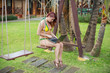 © Михаил Решетников - A young woman is sitting on a swing with a laptop. Work and travel. Cozy bungalows