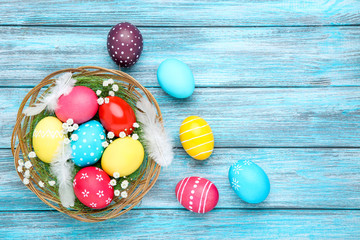 Wall Mural - Colorful easter eggs in basket with gypsophila flowers and feathers on wooden table