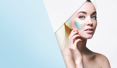 Portrait of beautiful woman with healthy glow perfect smooth skin look into the hole of blue paper. Young girl enjoys cream facial mask. Fashion, beauty, skincare, cosmetology concept.