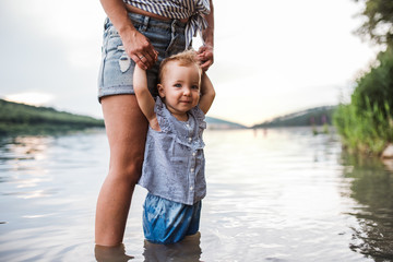 a midsection of mother with a toddler daughter outdoors by the river in summer.