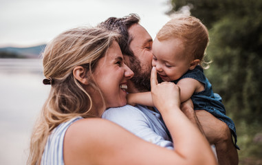a young family with a toddler girl outdoors by the river in summer.
