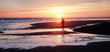 unrecognizable man walking on a deserted beach at sun set