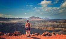 The Tourist Is Standing On The Edge Of The Rock And Looks At The Red Mountains In The National Park Timanfaya In Lanzarote