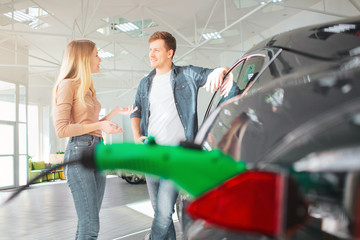 Young couple buying a first electric car in a showroom. Ecological vehicle concept. Modern technology in the automotive industry