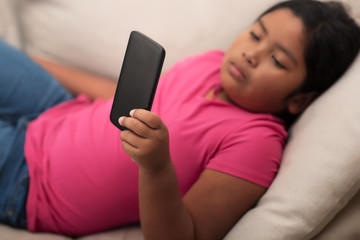 hispanic girl with a sad look on her face looking at a mobile phone unsupervised; resting on comfort