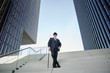 © Westend61 - Elegant businessman with bowler hat and walking cane, standing on stairs in the city