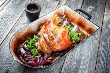 Traditionelle gegrillte bayrische Schweinshaxen mit Zwiebel als closeup in einem rustikalen Schmortopf auf altem hölzernen Board