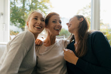 Happy Mother With Two Teenage Girls On Couch At Home