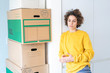 © Westend61 - Serious woman at home with cardboard boxes