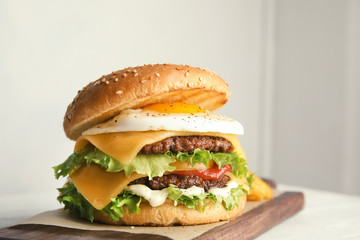 Tasty burger with fried egg on board against light background