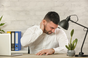 Tired young businessman suffering from neck pain in office after long hours at work