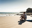 © Westend61 - Young woman sitting on her surfboard on the beach, looking at the sea