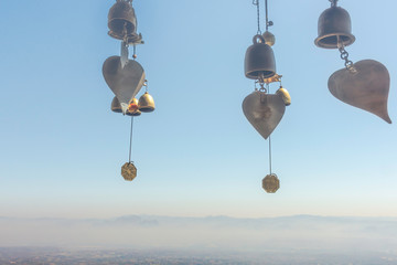 Brass bells hanging on blue sky with forest and mountains in fog on sunlight.