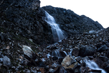 Wall Mural - Large mountain waterfall in the mountains on the dark wet rocks, evening landscape long exposure