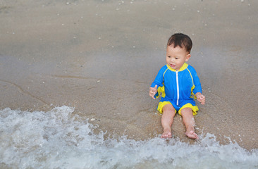 Portrait of Asian baby boy in swimming suit sitting on the sand beach.