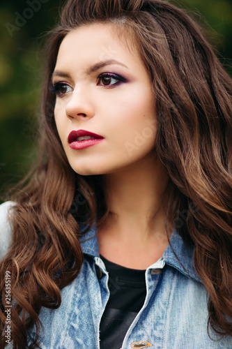 Portrait Of Stylish Beautiful Hipster Girl With Long Hair And Red Lips Walking At Street Holding Leather Bag And Sunglasses Gorgeous Smiling Brunette In Jeans Jacket And Black Top Posing Outdoor