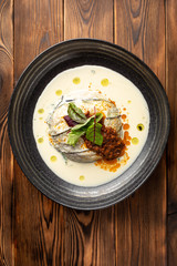 warm eggplant with spinach and parmesan milk in a black plate on a wooden background