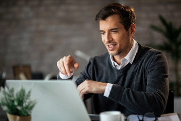 Smiling businessman surfing the net on laptop while working in the office.