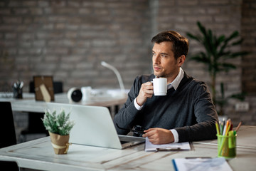 Thoughtful businessman drinking coffee and looking away while working at his desk.