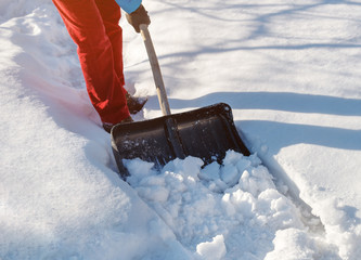 girl cleans snow shovel on the site near his house. sunlight