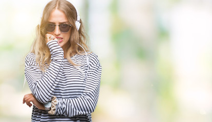 Poster - Beautiful young blonde woman wearing headphones and sunglasses over isolated background looking stressed and nervous with hands on mouth biting nails. Anxiety problem.