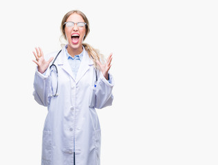 Canvas Print - Beautiful young blonde doctor woman wearing medical uniform over isolated background celebrating mad and crazy for success with arms raised and closed eyes screaming excited. Winner concept