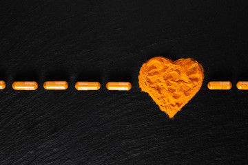 Wall Mural - Health care concept Turmeric spices powder in heart shape and capsule in black background