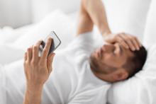 Technology And People Concept - Hand Of Young Man With Smartphone In Bed At Home In Morning