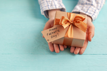 Wall Mural - Kid's hands holding gift box wrapped in craft paper and tied with bow.