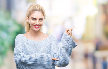 Sticker - Young beautiful blonde and blue eyes woman wearing winter sweater over isolated background with a big smile on face, pointing with hand and finger to the side looking at the camera.