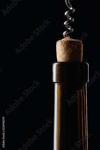 Fotografía Glass wine bottle with wooden cork and corkscrew isolated on black