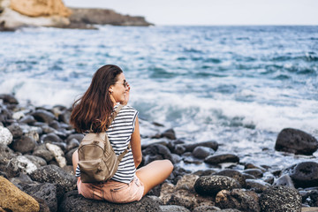 Wall Mural - Pretty long hair tourist girl relaxing on the stones near sea.