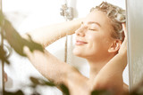 Beautiful satisfied European woman washes away shampoo from the head hair in bathroom, takes a shower and enjoys, smiling