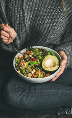 Wall Mural - Healthy vegetarian dinner. Woman in jeans and warm woolen sweater holding bowl with fresh salad, avocado, grains, beans, roasted vegetables. Superfood, clean eating, vegan, dieting food concept