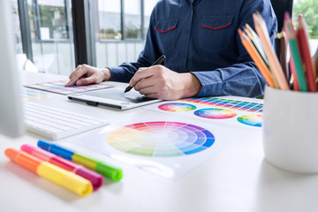 Poster - Male creative graphic designer working on color selection and color swatches, drawing on graphics tablet at workplace with work tools and accessories