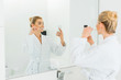 © LIGHTFIELD STUDIOS - selective focus of beautiful woman in white bathrobe brushing teeth and taking selfie in bathroom