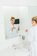 © LIGHTFIELD STUDIOS - woman in bathrobe applying toothpaste on toothbrush and looking at mirror