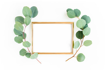 Gold frame is decorated with green branches and eucalyptus leaves on a white background. lay flat, top view