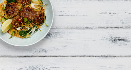 A bowl of succulent  Harissa Meat Balls on a bed of cuscus shot a white wooden background