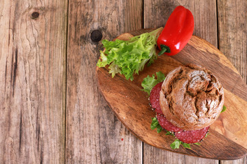 Wall Mural - whole-grain bun topped with salad and salami sausage - freshly baked whole grain bun breakfast on rustic wooden table 