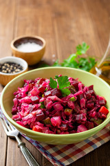 Wall Mural - Traditional russian salad vinaigrette with boiled vegetables, pickled cucumbers and sauerkraut in bowl on wooden table. Selective focus.