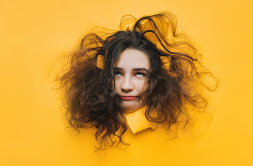 Skeptical emotions. A funny teenage caucasian girl with problematic dry curly hair expresses displeasure on her face. Orange, yellow paper background.