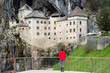© blazekg - Young woman is admiring the magnificent Predjama Castle which is one of the most famous landmarks in Slovenia, attracting  thousands of tourists each year.