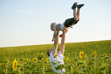 Wall Mural - Father throws up his little son on a green sunflowers field against the sky.