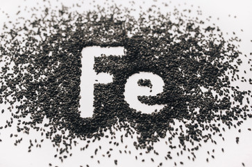 Chemical element - Fe. The word Ferrum in abbreviated form is written in black sesame seeds on a white background. The concept of healthy eating, iron, vegetarianism and metabolism. Close up.