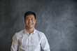 © mavoimages - Smiling Asian businessman standing in front of a blank chalkboard