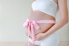 Close-up Pregnant Woman's Holding Belly With Pink Ribbon.