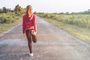 Shot of young fitness woman stretching legs before run on the long road. Woman warming up in the evening. Sport and Healthy concept. 