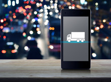 Truck Flat Icon On Modern Smart Mobile Phone Screen On Wooden Table Over Blur Colorful Night Light Traffic Jam Road With Cars In City, Business Service Transportation Online Concept