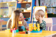 Kid and kindergarten teacher play with colorful wooden block toys on table